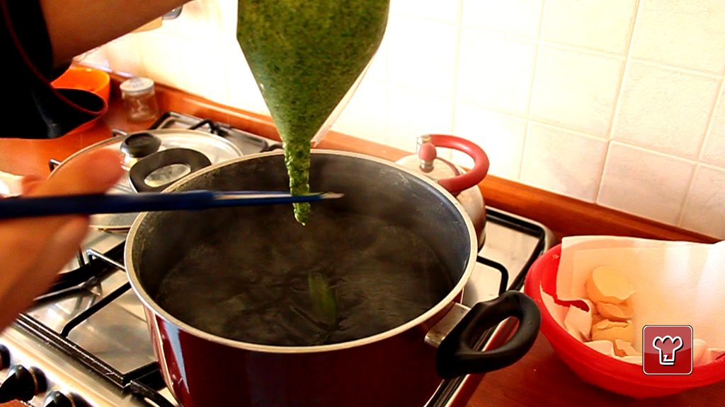 L impasto verde degli spatzli spremuto dalla sacca sopra la pentola e tagliato con una lama mentre scende