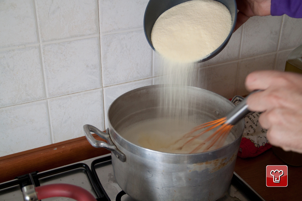 Il semolino versato a pioggia nel latte caldo mentre si mescola con la frusta