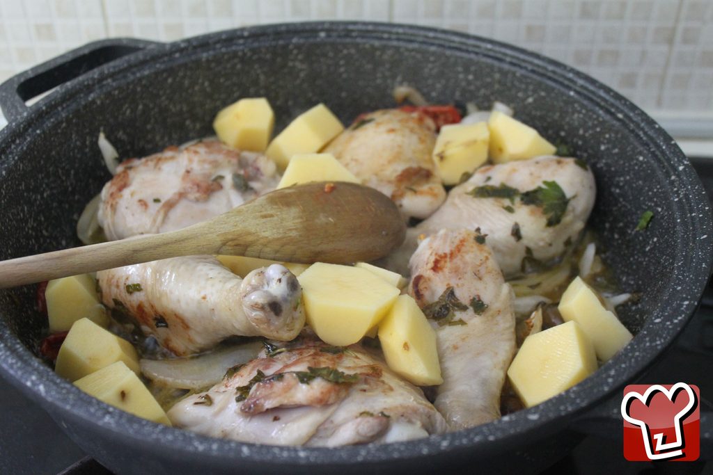 I pezzi grossi di patata aggiunti per ultimi nella padella, ancora chiari, fra i pezzi di pollo