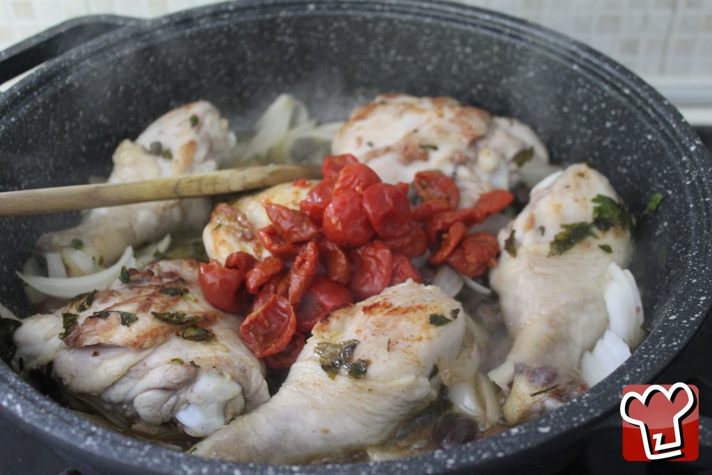 I pomodorini confit aggiunti nella padella insieme a olive e capperi, mescolati con il cucchiaio di legno