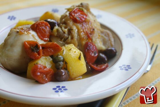 Il pollo in umido alla contadina servito nel piatto con le patate intere, le olive, i capperi e i pomodorini